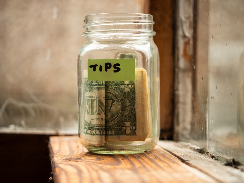 Ein Glas mit der Aufschrift "Tips", in welchem sich Geldscheine befinden