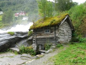 Blick auf eine Holzhütte, welche direkt neben dem Hellesyltfossen steht.