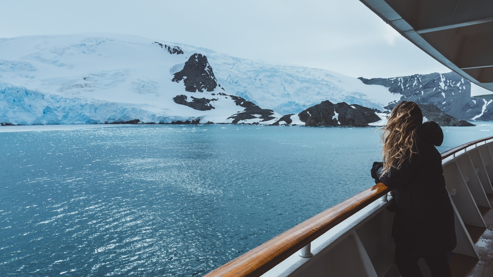 Eine Frau blickt von einem Kreuzfahrtschiff auf die antarktische Landschaft