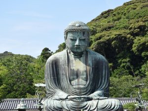 Bronzestatue des Großen Buddha (Daibutsu) in Kamakura, Japan, umgeben von üppigem Grün und klarem Himmel.