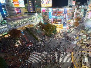 Blick auf die berühmte Shibuya-Kreuzung in Tokio bei Nacht, mit Menschenmengen, hellen Neonlichtern und umliegenden Hochhäusern voller Werbetafeln.