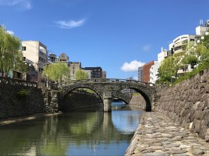 Historische Steinbrücke mit zwei Bögen über den Nakashima-Fluss in Nagasaki, umgeben von traditionellen Steinmauern und modernen Gebäuden